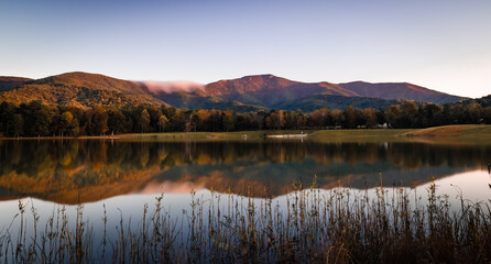 An autumn reflection of Shenandoah National Park in Lake Arrowhead as a fog bank rolls over the skyline at sunset.