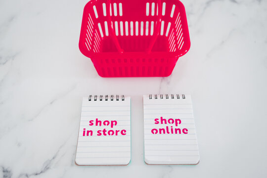 pink shopping baskets with shop in store vs shop online texts on notepads, competition and retail industry conceptual image