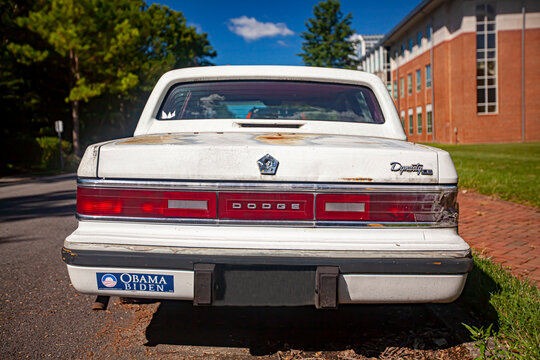 Chestertown, MD, USA 08/30/2020: Rear view of a very old white rusty Dodge Dynasty LE car parked outside on the street. It has rusted and chipped paint and a decade old Obama Biden bumper sticker