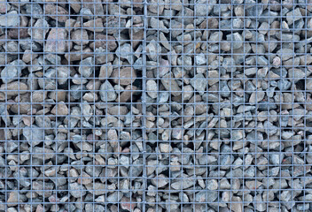 A gravel backfill wall behind a metal mesh.