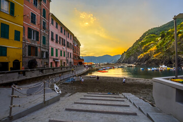 Obraz premium Children play along the sandy beach of Vernazza Italy harbor on the Cinque Terre as tourists enjoy a sunset dinner along the pier.