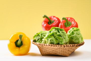 Fresh cos lettuce and bell peppers in a basket on white and yellow background