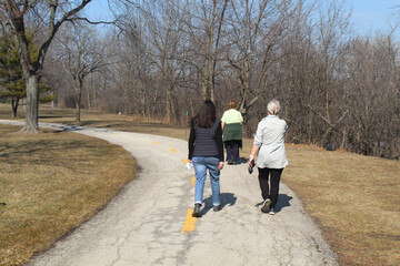 Fototapeta na wymiar Three older women walking on a trail at the Skokie Northshore Sculpture Park in Skokie, Illinois