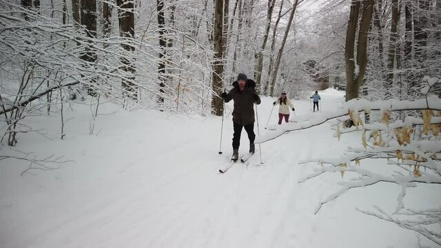 Family cross country skiing in a snow covered forest with a teen boy in front in slow motion.