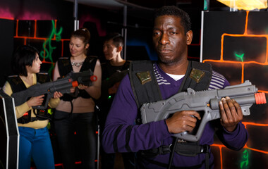 Portrait of confident adult African laser tag player with gun ready for game in dark labyrinth