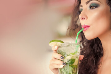 Young woman drinking mojito cocktail from mint soda light rum and lime with straw.
