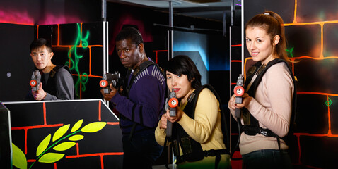 Fototapeta na wymiar Modern cheerful smiling people of different nationalities with laser pistols playing laser tag on dark labyrinth