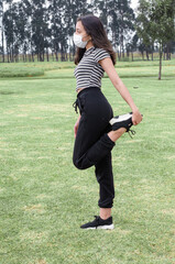 Fototapeta premium girl stretching her leg in the park wearing a mask