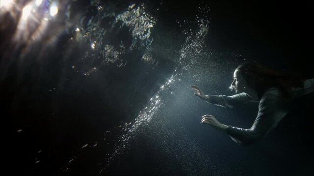mystery and magic underwater, young woman is floating to mirror water surface, rising over surface, subaquatic shot