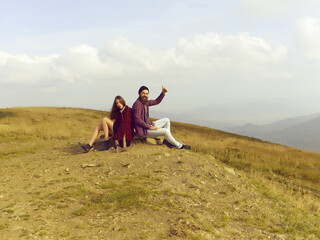 Fototapeta na wymiar Couple hipsters sitting on stone on mountain top on natural background.
