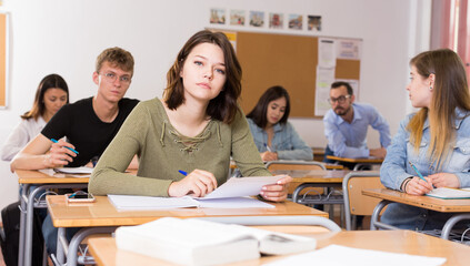 Obraz premium Young girl is writing test and thinking about questions at the desk in the class.