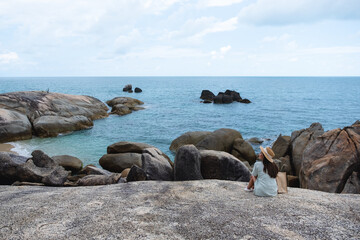 A young woman sitting on the rock by the sea