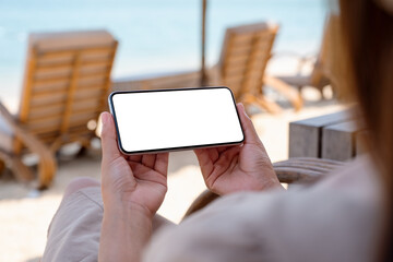 Mockup image of a woman holding mobile phone with blank desktop screen while sitting on the beach