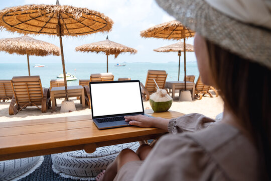 Mockup image of a woman using and touching on laptop touchpad with blank desktop screen while sitting on the beach