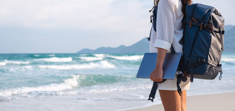 Closeup image of a female traveler holding laptop computer while walking on the beach