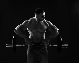 Fototapeta na wymiar Muscular strong men, athlete, bodybuilder, weightlifter does exercises with barbell for top and arms, looking at it in gym over dark background. Young man lifting weights. Black and white 