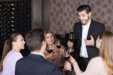 Young bearded man pronouncing toast on friendly meeting in cozy restaurant