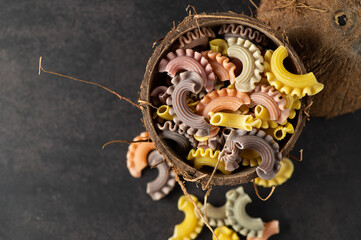 colored pasta in the form of handmade scallops in a coconut plate on a gray vintage background, top view