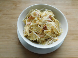pasta farfalle with mushrooms, cheese and bacon in a white plate on a wooden table.