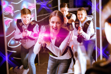 Obraz na płótnie Canvas Portrait of young woman with laser gun having fun on dark lasertag arena