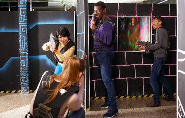 Modern glad people of different nationalities with laser pistols playing laser tag on dark labyrinth