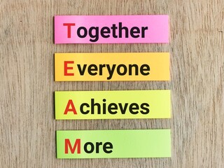 Team concept.Phrase TOGETHER EVERYONE ACHIEVES MORE written on colorful sticky note isolated on wooden background.