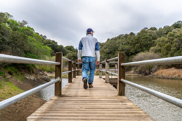 A man, visitor, hiker walking away low on a pier or a wharf over a small lake with tree covered trees on both sides and cloudy sky overhead, Waterdog Lake, Belmont, California