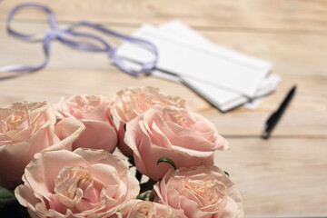 Closeup pink rose flower bouquet and blank empty copy space paper pile with pen, silk ribbon on...