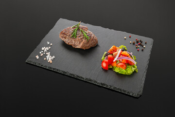 Grilled beef steak with vegetable salad. On a black slate board. Dark background. Isolated. Close-up.