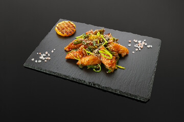 Pike perch fillet with eggplant and oyster sauce. On a black slate board. Decorated with coarse sea salt and a slice of lemon. Dark background. Isolated