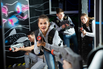 Fototapeta na wymiar Portrait of excited woman holding laser gun in arena, playing laser tag game with friends. High quality photo