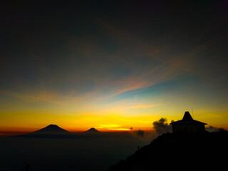 
The view of the twilight from the top of the mountain with an orange sky and a tomb building on the mountain
