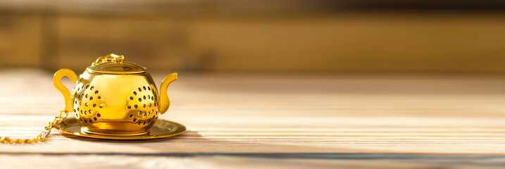Vintage tea strainer on a wooden table with a dream for text. Teapot-shaped golden tea strainer