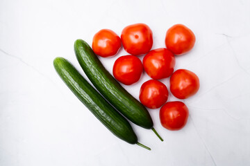 Green cucumbers and red tomatoes on the kitchen marble table.