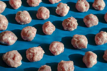 Raw shaped meatballs in sunbeams on blue.
