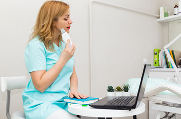 Smiling young female doctor wearing blue medical uniform consulting patient online on laptop, happy positive Caucasian woman nurse or physician working using modern laptop in clinic or hospital