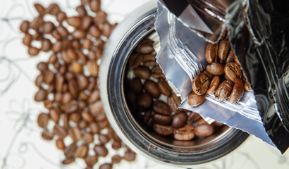 A packet of coffee beans against the background of an electric coffee grinder and a blurry handful of coffee beans on the table