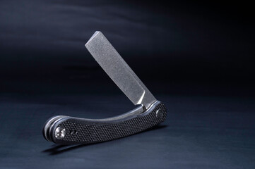 An unusual knife with a blunt edge. The knife is in the flat-folded position. Knife ax on a black...