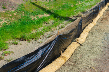 Straw wattles and plastic fence placed along dry creek to reduce soil erosion, debris runoff and retain sediment during construction and maintenance project.