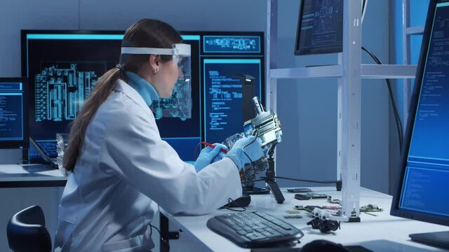 Female microelectronics engineer works in a modern scientific laboratory on computing systems and microprocessors. Electronic factory worker is testing the motherboard and coding the firmware.