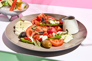 Tomato, olives and mozzarella salad . Restaurant appetizer plate on white table with pink wall. Day sunlight with hard shadow of fern palm leaves. Summer or spring restaurant food concept