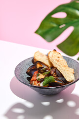 Mussel with bread restaurant plate. Restaurant appetizer plate on white table with pink wall. Day sunlight with hard shadow of monstera palm leaves. Summer or spring restaurant food concept.