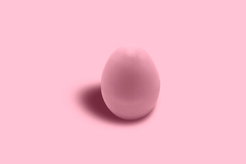 A chicken egg painted pink in close-up on a pink background. Free space. Minimalism. Pink on pink.