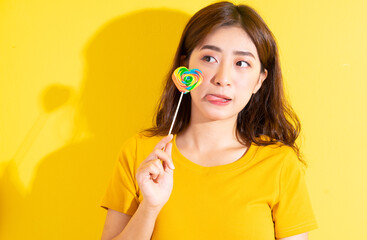 Young Asian woman eating lollipop on yellow background