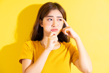 Young Asian woman eating lollipop on yellow background
