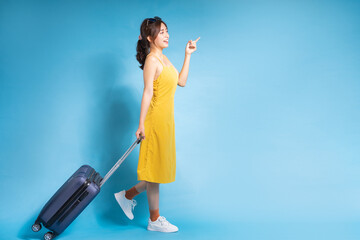 Young Asian woman holding suitcase on blue background, summer concept