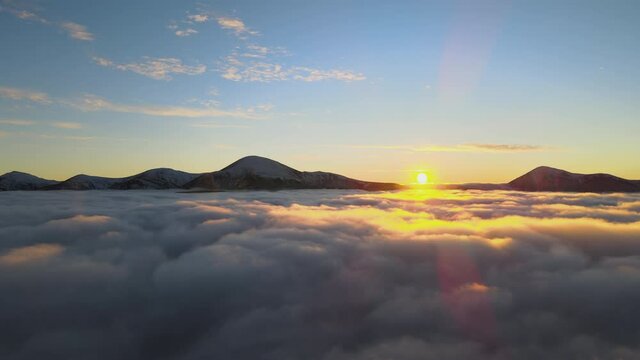 Aerial view of vibrant sunrise over white dense fog with distant dark peaks of Carpathian mountains on horizon.