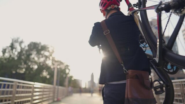 Back tracking view of an environmentalist in formal cloths carrying his bicycle to workplace, smart handsome cyclist traveling by sustainable transport and living a healthy lifestyle, save planet