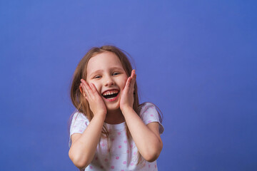 Little girl 5 years old with blonde hair in a T-shirt with colored polka dots standing happily smiling on purple background. Close-up. the model is having fun and feels overwhelmed, amazed.
