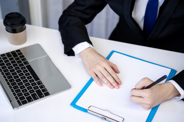 Asian business man dringking coffee wearing suit, enjoying watching educational webinar on laptop or laptop and smartphone. Smiling with chat and holding video call with clients partners.